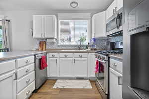 Kitchen featuring appliances with stainless steel finishes, a sink, white cabinets, backsplash, and light countertops