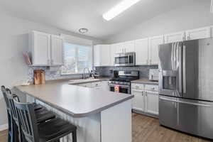 Kitchen featuring stainless steel appliances, a sink, tasteful backsplash, a breakfast bar area, and lofted ceiling