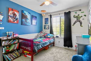Bedroom featuring multiple windows, wainscoting, carpet flooring, and a ceiling fan