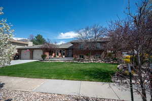 Split level home with an attached garage, a front lawn, brick siding, and concrete driveway