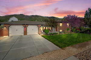 View of front of home with a mountain view, a garage, concrete driveway, a lawn, and brick siding
