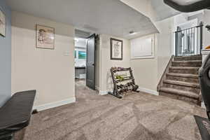 Basement with baseboards, carpet floors, stairway, and a textured ceiling