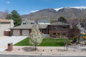 Split level home with a garage, concrete driveway, a mountain view, and brick siding