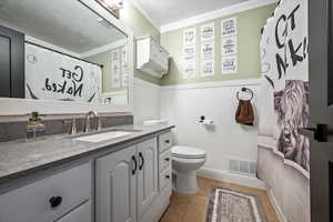 Full bath with a textured ceiling, wainscoting, vanity, ornamental molding, and tile patterned flooring