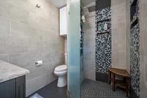 Bathroom featuring tile walls, a stall shower, toilet, vanity, and tile patterned flooring