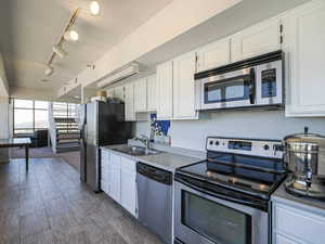 Sky Room Kitchen with stainless steel appliances, a sink, white cabinets, and track lighting