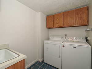 Laundry area with cabinet space, washer and dryer, dark tile patterned floors, a textured ceiling, and baseboards