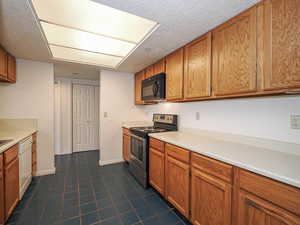 Kitchen with stainless steel electric range oven, black microwave, white dishwasher, brown cabinets, and a textured ceiling