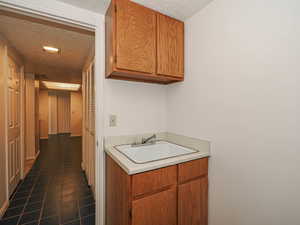 Hall featuring a textured ceiling, a sink, and dark tile patterned flooring