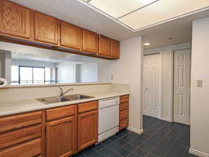 Kitchen with white dishwasher, a sink, dark tile patterned floors, brown cabinetry, and light countertops