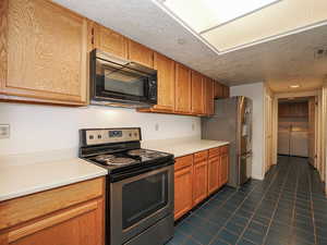 Kitchen featuring appliances with stainless steel finishes, washing machine and dryer, dark tile patterned flooring, light countertops, and a textured ceiling