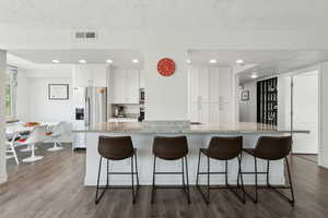 Kitchen with appliances with stainless steel finishes, white cabinetry, dark wood-type flooring, a kitchen bar, and recessed lighting