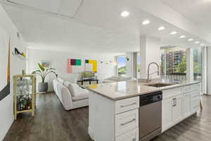 Kitchen featuring stainless steel dishwasher, a sink, open floor plan, baseboards, and light stone counters