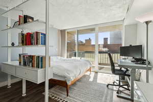 Bedroom featuring wood finished floors, access to exterior, floor to ceiling windows, and an office area
