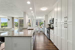 Kitchen featuring appliances with stainless steel finishes, a sink, a textured ceiling, a center island with sink, and open floor plan