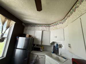 Kitchen with a textured ceiling, freestanding refrigerator, light countertops, white cabinets, and a sink