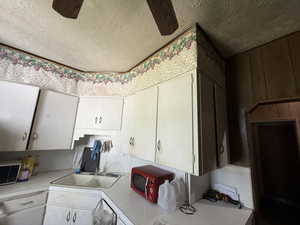 Kitchen featuring light countertops, a textured ceiling, a sink, white cabinets, and a ceiling fan