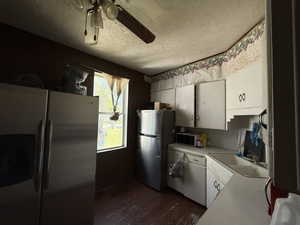Kitchen featuring stainless steel refrigerator with ice dispenser, freestanding refrigerator, a textured ceiling, dark wood-style flooring, and white cabinets