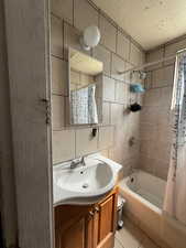 Bathroom with tile patterned floors, shower / bathtub combination with curtain, vanity, tile walls, and toilet