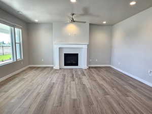 Unfurnished living room with ceiling fan, wood finished floors, recessed lighting, a brick fireplace, and baseboards