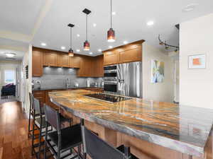 Kitchen featuring stainless steel appliances, stone countertop, a kitchen breakfast bar, and a sink in the bar/island.