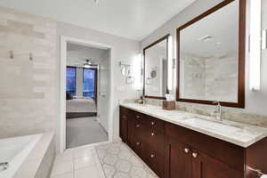 Bathroom featuring double vanity, tile patterned floors, ensuite bathroom, tiled tub, and ceiling fan