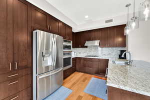 Kitchen featuring appliances with stainless steel finishes, under cabinet range hood, a sink, light wood-style flooring, and tasteful backsplash