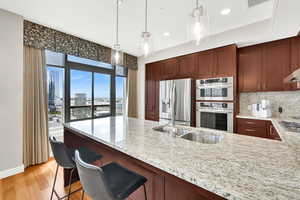 Kitchen featuring appliances with stainless steel finishes, light wood finished floors, light stone countertops, pendant lighting, and a peninsula