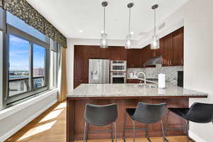 Kitchen with appliances with stainless steel finishes, under cabinet range hood, a sink, a peninsula, and decorative backsplash