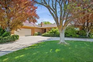 View of front facade with brick siding, an attached garage, a front yard, a chimney, and driveway