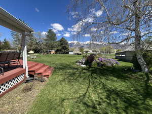 View of grassy yard with a deck with mountain view