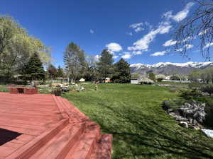 View of grassy yard with a deck with mountain view
