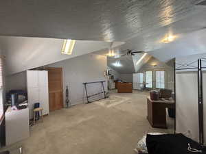 Additional living space with vaulted ceiling, ceiling fan, light carpet, a textured ceiling, and baseboards