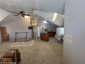 Additional living space with vaulted ceiling, light colored carpet, ceiling fan, and a textured ceiling
