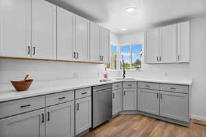 Kitchen with stainless steel dishwasher, a sink, a textured ceiling, light wood-style flooring, and gray cabinets