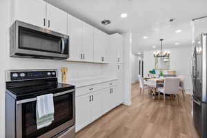 Kitchen with stainless steel appliances, white cabinets, a chandelier, light wood finished floors, and light countertops
