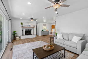 Living room with a ceiling fan, light wood-style floors, recessed lighting, ornamental molding, and a fireplace