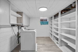 Washroom with washing machine and clothes dryer, light wood-style flooring, wooden walls, and wood ceiling