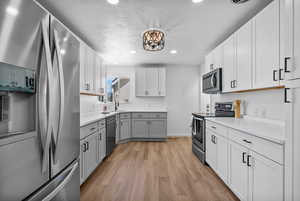 Kitchen with stainless steel appliances, light wood-style flooring, light countertops, recessed lighting, and gray cabinets