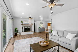 Living area featuring ceiling fan, recessed lighting, light wood-type flooring, ornamental molding, and a brick fireplace