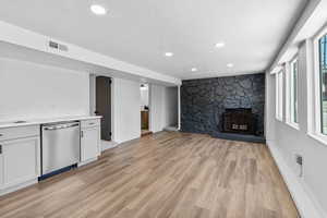 Unfurnished living room with a textured ceiling, light wood finished floors, a stone fireplace, recessed lighting, and baseboards