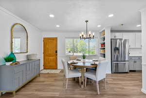 Dining area featuring light wood finished floors, plenty of natural light, recessed lighting, a chandelier, and ornamental molding