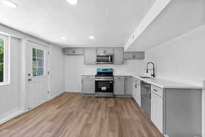 Kitchen with gray cabinetry, stainless steel appliances, a sink, a textured ceiling, and light wood finished floors