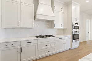 Kitchen featuring custom exhaust hood, stainless steel appliances, light wood-style floors, backsplash, and recessed lighting