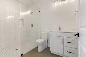 Bathroom with a walk in shower, vanity, tile patterned flooring, and toilet