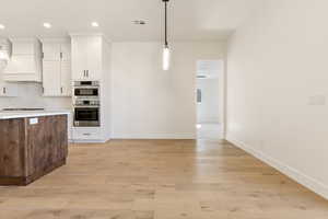 Kitchen with custom exhaust hood, white cabinetry, baseboards, pendant lighting, and recessed lighting
