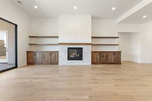 Unfurnished living room with light wood-style flooring, recessed lighting, baseboards, and a tiled fireplace
