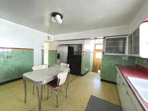 Kitchen featuring a sink, a wainscoted wall, white cabinets, glass insert cabinets, and stainless steel fridge with ice dispenser