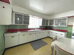 Kitchen featuring a sink, white cabinetry, glass insert cabinets, tile walls, and backsplash