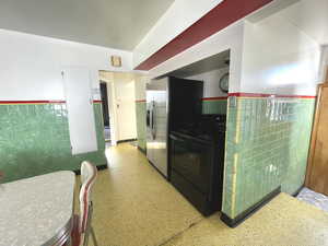 Kitchen featuring black electric range, tile walls, dark aggregate flooring, a wainscoted wall, and stainless steel fridge with ice dispenser